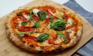 Pizza z pikantnym salami, pomidorkami, rukolą i bazylią na drewnianej desce.