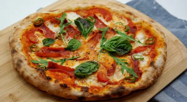 Pizza z pikantnym salami, pomidorkami, rukolą i bazylią na drewnianej desce.