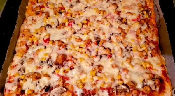 Prostokątna pizza z kurczakiem, kukurydzą, papryką i serem.