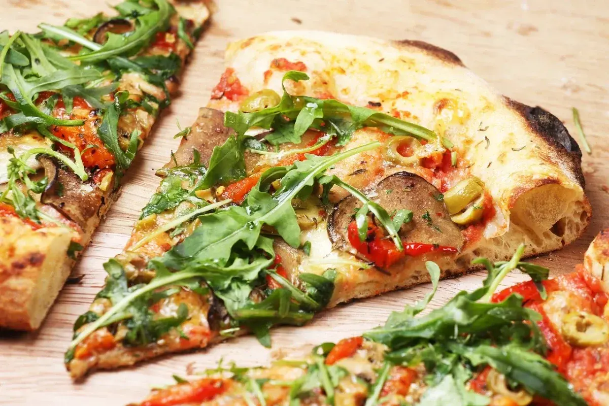 Kawałki pizzy z rukolą, oliwkami i warzywami na drewnianym tle.